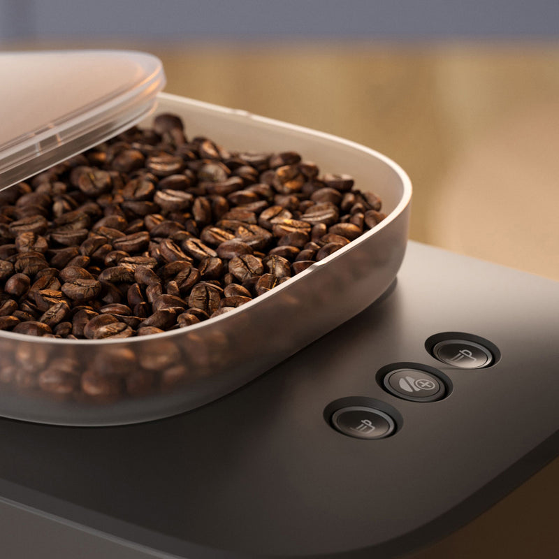 A close-up of the Philips Baristina Combo Espresso Machine with Milk Frother BAR303/60's bean container, filled with freshly ground beans. The container is slightly open, and three buttons featuring different coffee-related icons are visible on the machine's surface next to it. The background is blurred.