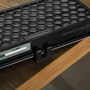 The black Miele Active AirClean filter with TimeStrip SF-AA 30, characterized by its hexagonal pattern, is resting on a wooden surface. This Miele filter incorporates active charcoal and features a small latch on the side, along with a label that shows part of a website URL.