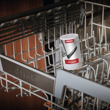 A tube of Miele DishClean Dishwasher Conditioner 160g GP CO G 160 P is positioned upright in the top rack of an open dishwasher, showcasing its appliance performance. The interior features shiny metal racks and a handle with the brand name "Miele" partially visible in the foreground, reflecting exceptional dishwasher cleaning.