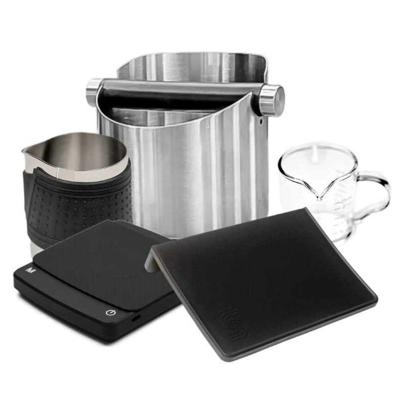 The Barista Bundle from HCS includes a stainless-steel knock box with a black rubber-coated bar, a frothing pitcher with a black heat sleeve, and a glass measuring cup. It also features two Barista Scales, one with an angled design for precise coffee creations. These items are thoughtfully arranged against a white background.