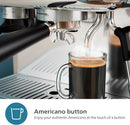 A close-up of the Philips Barista Brew Semi Automatic Espresso Machine PSA3218/01 (Silver) with a stainless steel portafilter, dispensing freshly brewed Americano into a clear glass mug. Steam rises from the cup. The caption reads, "Americano button - Enjoy your authentic Americano at the touch of a button.