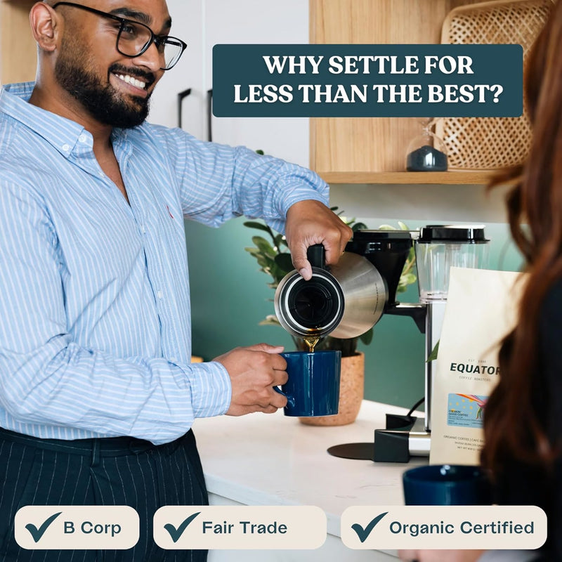 A man pours medium-dark roast coffee into a blue mug in a modern kitchen. A sign above him reads, "Why settle for less than the best?" Icons show B Corp and Fair Trade certifications. A bag of Equator Coffee Roasters Freakin’ Good Coffee Bean (908g / 2lb) rests on the counter.