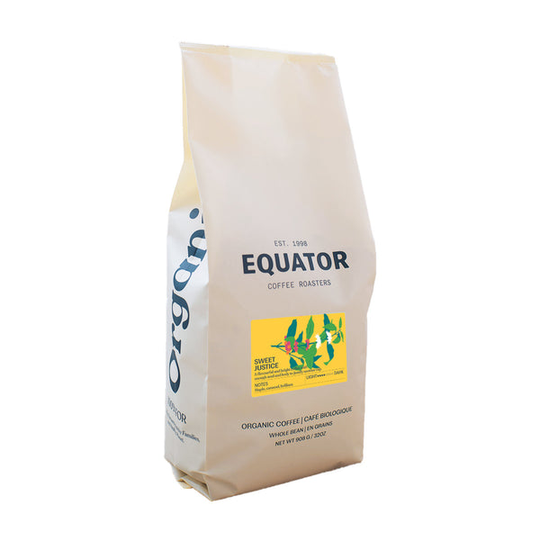 A beige Equator Coffee Roasters bag, featuring a yellow label with a green hummingbird graphic, showcases "Sweet Justice." This locally roasted, fair trade coffee promises rich taste.