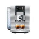 A sleek, aluminum white Jura Z10 Super Automatic Hot Coffee & Espresso Machine is shown with a digital screen on top displaying various coffee options. Below the screen, two freshly brewed espresso shots are positioned side by side, ready to serve. The Swiss engineering ensures precision and quality in every cup.