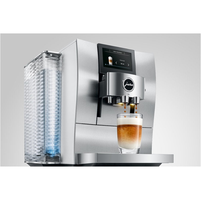 The Jura Z10 Aluminum White Super Automatic Hot Coffee & Espresso, Cold Brew, & Specialty Beverage Machine - DEMO (4082) is dispensing a layered coffee into a clear glass. This modern machine features a beautifully textured water reservoir on the left side and boasts a touch screen interface that highlights cold brew specialties. The Product Recognising Grinder (P.R.G.) ensures optimal flavor extraction from every grind.