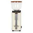 The ECM C-Manuale 54 Burr Grinder by ECM features a cream-colored finish with a transparent hopper and a wooden lid. This grinder offers manual grinding capabilities with adjustable grind settings. It includes a metal handle on the front and control switches on the side, all standing upright against a white background.