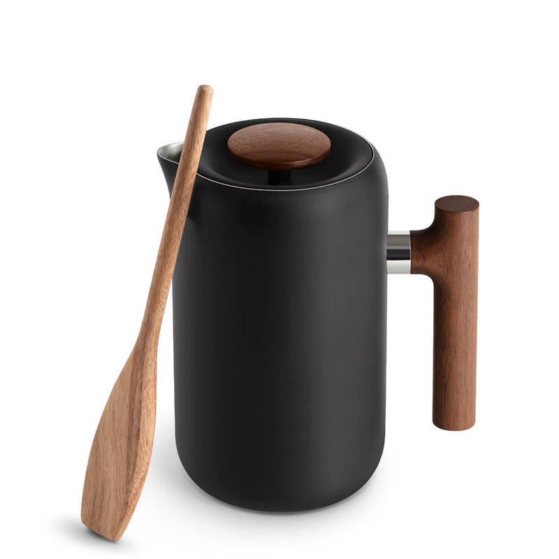 Introducing the Fellow Clara French Press (Matte Black + Walnut), a sleek piece of barista-level equipment. This black ceramic press features a polished wooden lid and handle, complemented by a matching walnut paddle spoon. The minimalist design juxtaposes its matte black body with natural wood accents, all elegantly presented against a plain white background.