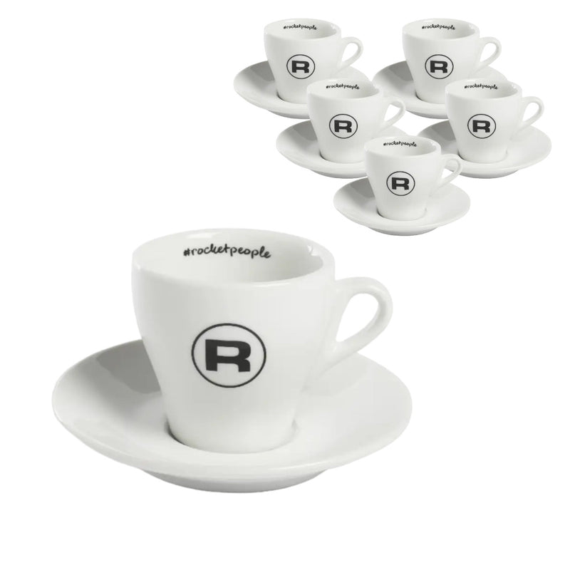 [Intro]
The Rocket Espresso Cups Hashtag Series - Set of 6 RA99907206 (White) by Rocket features elegant white ceramic espresso cups and saucers, each adorned with a distinctive black "R" logo. A set of six cups and saucers is displayed, highlighted by an enlarged view of one cup and saucer in the foreground. The inside of the cups showcases the text "