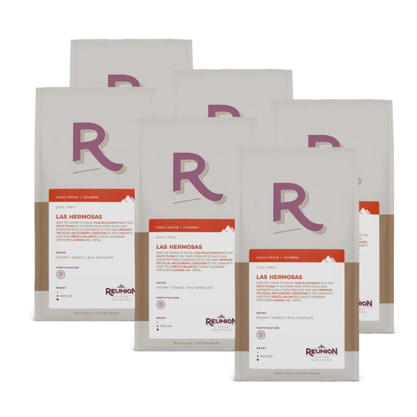 Six white and brown coffee bags are displayed. Each bag features a large "R" logo and reads "Reunion Island Colombian Las Hermosas," indicating a Colombian coffee from the South Tolima region. Descriptive text about the Fair Trade Certified coffee's origin and flavor notes appears below the main label, showcasing Reunion Coffee Roasters' commitment to quality.