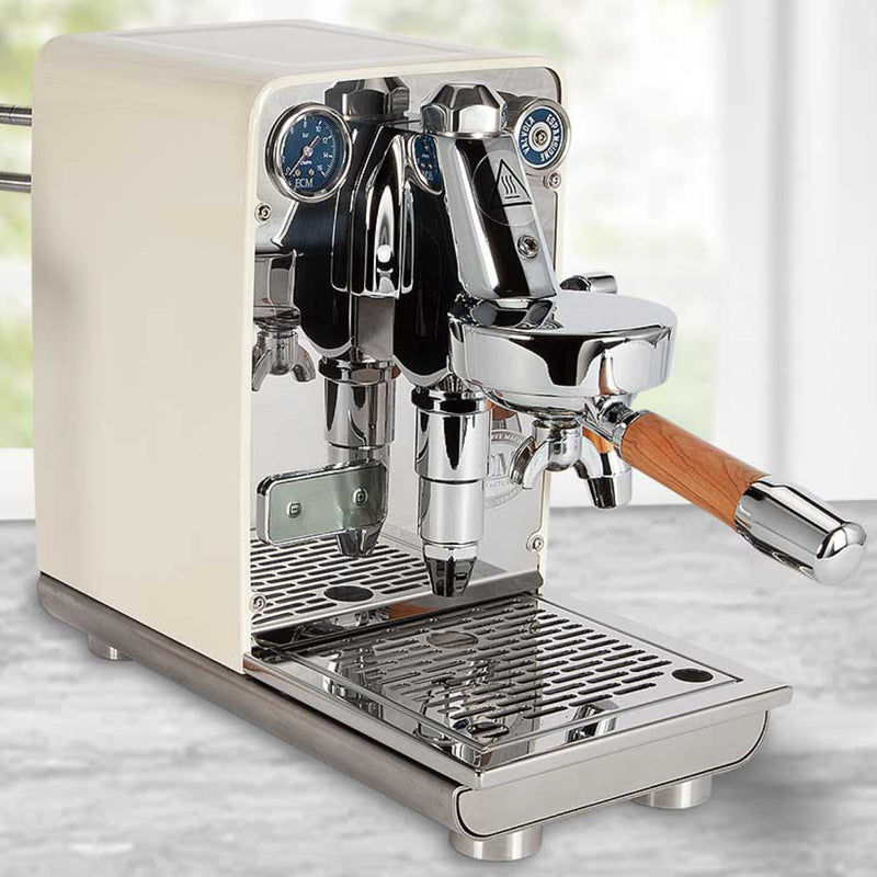 A stylish cream ECM Puristika Semi Automatic Espresso Machine is elegantly positioned on the countertop, showcasing chrome accents and a wooden-handled portafilter alongside dual pressure gauges. Its stainless steel boiler guarantees durability, while a blurred window view in the background enhances its sophisticated appearance.