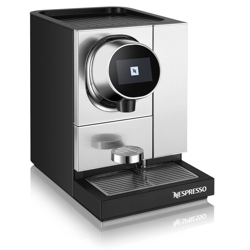 A sleek, modern Nespresso Momento 100 Commercial Coffee Machine with a black and silver design. This Nespresso machine features capsule recognition and a digital display, along with a single spout for dispensing coffee. It has a drip tray at the bottom and boasts compact, angular construction.