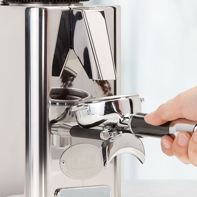 An expert hand skillfully operates the ECM S-Automatik 64 Burr Grinder, efficiently filling a portafilter with freshly ground coffee. This sleek stainless steel device features a modern design and prominently showcases its ECM brand logo. In the softly blurred background, the aroma of perfectly dosed coffee permeates the air.