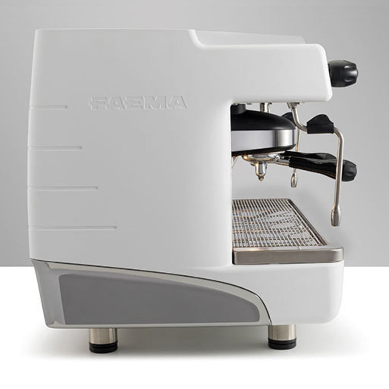 A side view of the Faema E98UP 2 Group Head Espresso Machine F01-UL210VWTB999A in sleek, modern white with silver accents. The brand name "FAEMA" is embossed on the side. The machine features a portafilter, steam wand, and drip tray, standing on four short legs with metallic finishes. Its ergonomic and robust design includes a fixed-nozzle thermosyphon system. The background is plain gray.