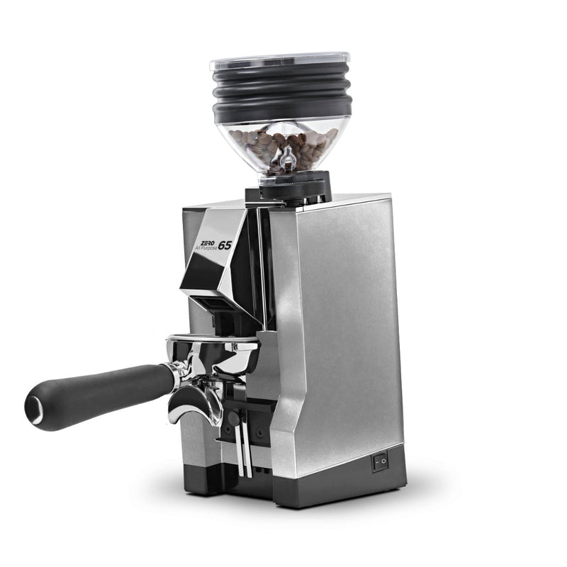 The Eureka Mignon Zero 65 All Purpose Grinder by Eureka, featuring a sleek chrome finish, displays a transparent bean hopper filled with coffee beans on its anti-vibration system. The grinder boasts a front portafilter and 65 mm flat burrs and is slightly angled to highlight its cutting-edge design.