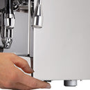 Close-up of a hand adjusting a stainless-steel knob beneath an ECM Mechanika VI Slim Espresso Machine - Demo, Unused. The shiny spouts and dials of the ECM appliance are visible in the top-left corner, reflecting light and emphasizing its polished finish.