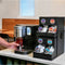 A person is making iced coffee using the "Strong Brew" option on a Keurig K2550 K-Cup® Commercial Brewing System on a kitchen counter. Next to the coffee maker is a black organizer filled with various pod flavors. A wooden bench and table are visible in the background.