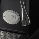 A close-up of the ECM Synchronika Espresso Machine - Dual Boiler w/ PID (Black) (Special Edition) from ECM highlights a metal logo plaque with the words "Espresso Coffee Machines" and "Heidelberg, Germany" around the company initials. The image also showcases the E61 Group Head, portafilter area, and drip tray of this dual boiler espresso machine.