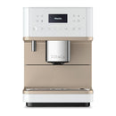 A modern Miele CM6360 Super Automatic Countertop Coffee & Espresso Machine in Lotus White with a sleek design, featuring a digital display, silver accents, and a built-in milk frother. The machine has various buttons for settings and functionalities, with the Miele logo prominently displayed on the front.