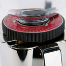 Close-up of the ECM C-Manuale 54 Burr Grinder by ECM, highlighting its on-demand coffee grinding capabilities with a distinctive red adjustment dial adorned with white numbers and surrounded by a black ridged outer ring. The grinder's shiny, reflective stainless steel body emphasizes the manual grinding mechanism, drawing attention to the top section that features part of its transparent hopper.