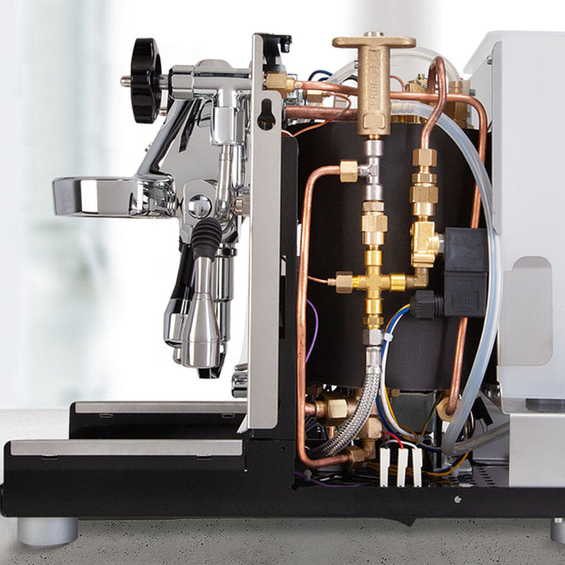 The image reveals an exposed internal view of the ECM Mechanika VI Slim Espresso Machine - Demo, Unused. Various metal components, copper pipes, and electrical wiring are visible, highlighting the intricate mechanics within this coffee brewing and milk frothing marvel. The outer casing has been partially removed to expose the detailed stainless steel construction inside this impressive ECM machine.