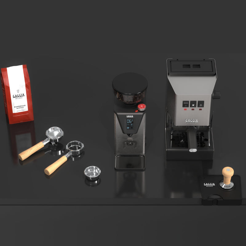 A coffee brewing setup on a black surface, featuring a bag of coffee beans, a Gaggia MDF 55 Grinder with Silent-Grind Technology, a portafilter with wooden handle, two metal filter baskets, an espresso machine, and a tamper.