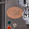 Close-up of an espresso machine featuring a copper label that reads "Espresso Coffee Machines ECM Manufacture Heidelberg Germany." The ECM-customized E61 group head highlights switches and indicator lights in red, green, and orange, enhancing the sleek design of the Mechanika VI Slim Espresso Machine Heritage Line by ECM.