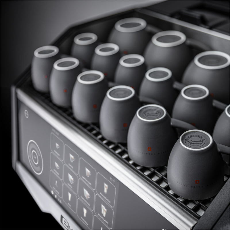 A close-up image of the Eversys Cameo Steam Wand Classic Espresso Machine C'2s (Tempest) by Eversys showcases several small black cups neatly arranged in rows on top. The machine's control panel, displaying various coffee options, is slightly visible in the lower left corner of the image, while the steam boiler subtly hints at its power for perfect Latte Art.