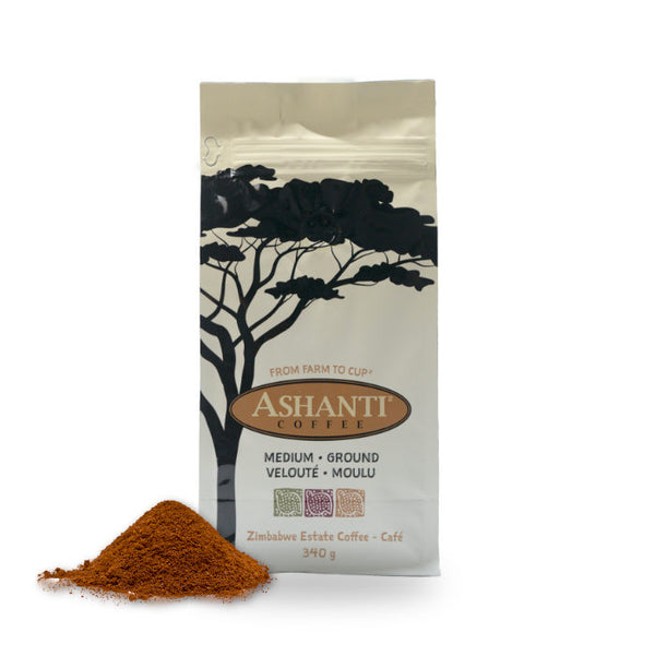 A bag of Ashanti Artisan Coffee African Medium Roast Ground Coffee from Ashanti Coffee sits against a white background. The package features a tree silhouette design and text that reads "From Farm to Cup," "Medium Ground," and "Zimbabwe Estate Coffee." Beside the bag is a small pile of medium ground coffee, hinting at subtle notes of caramel chocolate orange.