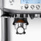 Close-up of the grinder section of the Breville The Barista Pro Espresso Machine BES878 / BES878OLT (Olive Tapenade). Freshly ground coffee is visible in the portafilter positioned under the grinder. Buttons, an intuitive LCD interface, and control dials are seen at the top part of the machine, along with a powerful ThermoJet heating system.