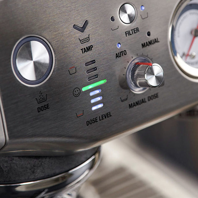 Close-up of the Breville The Barista Express Impress Semi-Automatic Espresso Machine BES876OTL control panel. Visible are a large knob, buttons labeled "Tamp," "Auto," "Manual," "Dose," and "Filter," alongside an indicator light on "Dose Level." A pressure gauge is partially visible on the right, showcasing assisted tamping and automatic dosing features.