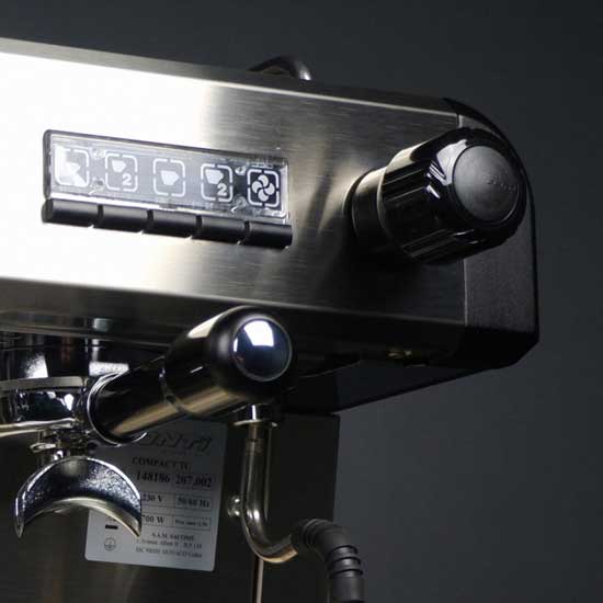 A close-up view of the Conti CC100 1 Group Espresso Machine in elegant black stainless steel showcases its sophisticated control knobs and buttons. The portafilter is secured beneath an interface adorned with icons and lights. Expertly engineered for flawless coffee extraction, this machine is set against a dark background for emphasis.