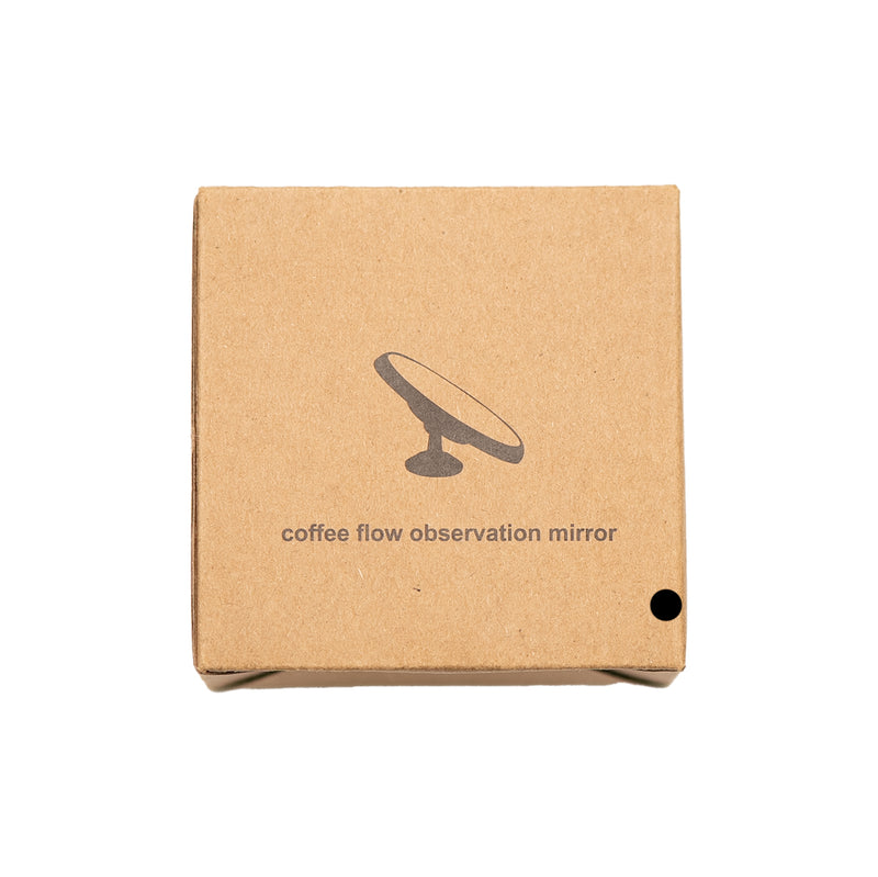 A brown cardboard box with the text "HCS Espresso Shot Mirror" printed on it in lowercase letters. An illustration of a mirror on a stand is above the text. Perfect for channeling detection and espresso shot analysis, there's also a small black dot in the bottom-right corner of the box.