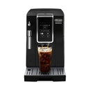 The black DeLonghi Dinamica Super Automatic Espresso & Coffee Machine - ECAM35020B (Open Box, Unused) features a digital display screen and button controls. It dispenses iced coffee into a tall glass filled with ice cubes on the drip tray. A frothing wand is visible on the left side, showcasing its versatile iced coffee functionality.