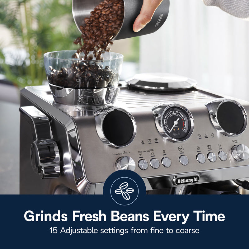 A person pours coffee beans into the grinder on a stylish DeLonghi La Specialista Maestro Espresso Machine with Cold Brew EC9885M in silver. This machine features various knobs and buttons along with a pressure gauge. Text overlay reads "Grinds Fresh Beans Every Time" and highlights "15 Adjustable Settings from Fine to Coarse.