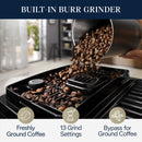 Close-up of the built-in burr coffee grinder on the DeLonghi Magnifica Start Super Automatic Espresso Machine ECAM22022B (Black) with roasted coffee beans being poured into it. The image highlights features such as integrated grinding technology for freshly ground coffee, 13 grind settings, and a bypass for ground coffee—ideal for crafting exquisite coffee drinks.