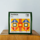 A green coffee bag from Ethica Coffee Roasters, labeled "Rwanda Muzo Washed Whole Bean Coffee (250g)," features decorative geometric patterns in yellow, red, blue, and orange. The label highlights flavor notes of "Stone Fruits, Honey, Citrus," making it perfect for filter coffee. The bag is placed on a wooden surface against a plain background.