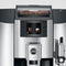 The Jura E8 Chrome Automatic Coffee Machine 15371 OPEN BOX (4033) is a modern espresso machine featuring a digital display that presents various coffee drink options. It has an integrated coffee grinder visible through a transparent compartment that showcases the coffee beans. The sleek silver-colored control panel and spouts, along with the Pulse Extraction Process (P.E.P.), guarantee perfect shots every time.