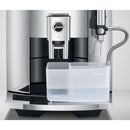 A chrome Jura E8 Automatic Coffee Machine (model 15371) with an attached transparent water container. The machine features a central coffee spout, a side milk frother, and utilizes the Pulse Extraction Process (P.E.P.) to make perfect coffee. This open-box unit is in excellent condition and shows a soft stream of water being dispensed into the container.