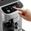 A hand touches the display of the DeLonghi Magnifica Plus Super Automatic Espresso Machine with LatteCrema System (ECAM32070SB), selecting a cappuccino from 18 coffee drinks. Featuring a sleek silver design and built-in milk frother, it also boasts LatteCrema Hot technology for perfectly crafted beverages every time.