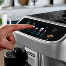 Close-up of a person’s hand selecting a coffee option on the touch screen of a DeLonghi Magnifica Plus Super Automatic Espresso Machine with LatteCrema System (ECAM32070SB). Various choices like cappuccino, espresso, and one of the 18 available coffee drinks are displayed. A coffee cup is positioned below the machine's spout.