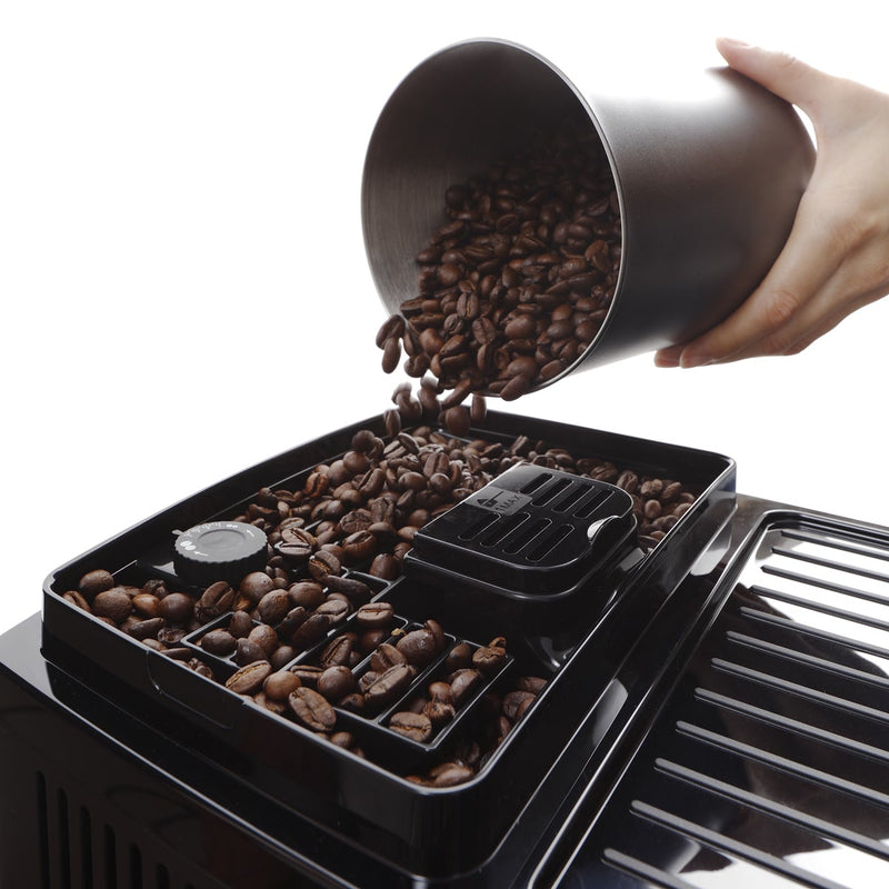 A hand pours coffee beans into the bean compartment of the DeLonghi Magnifica Start Super Automatic Espresso Machine with LatteCrema System ECAM22080B, initiating a customizable experience. The machine's black, sleek surface contrasts beautifully with the rich, dark coffee beans, making it perfect for crafting exquisite coffee drinks.