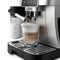 The DeLonghi Magnifica Start Super Automatic Espresso Machine with LatteCrema System ECAM22080SB (Silver) by DeLonghi creates coffee beverages as dual spouts pour espresso into a glass cup, which is layered with milk and froth using its LatteCrema System. The milk frother attachment sits on the black drip tray, offering a personalized experience.