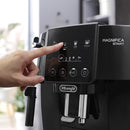 A person is pressing a button on the stylish DeLonghi Magnifica Start Super Automatic Espresso Machine ECAM22022B in black. The control panel, equipped with integrated grinding technology, provides options such as Espresso, Coffee, and Americano. This modern marvel is ideal for creating your favorite coffee drinks.