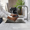 A person washes a black camera under running water in a modern kitchen. There's a large metal sink, a tall faucet, and a plant in the background. The counter is white and clean, reminiscent of the pristine setup for preparing coffee drinks with the DeLonghi Magnifica Start Super Automatic Espresso Machine with LatteCrema System ECAM22080B.