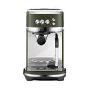 A compact Breville The Bambino Plus Espresso Machine BES500OTL (Olive Tapenade), in a striking green and silver color, is shown against a white background. This machine, equipped with a portafilter, steam wand, control buttons, and drip tray, boasts barista-quality microfoam capabilities and features a clear water reservoir on the back.