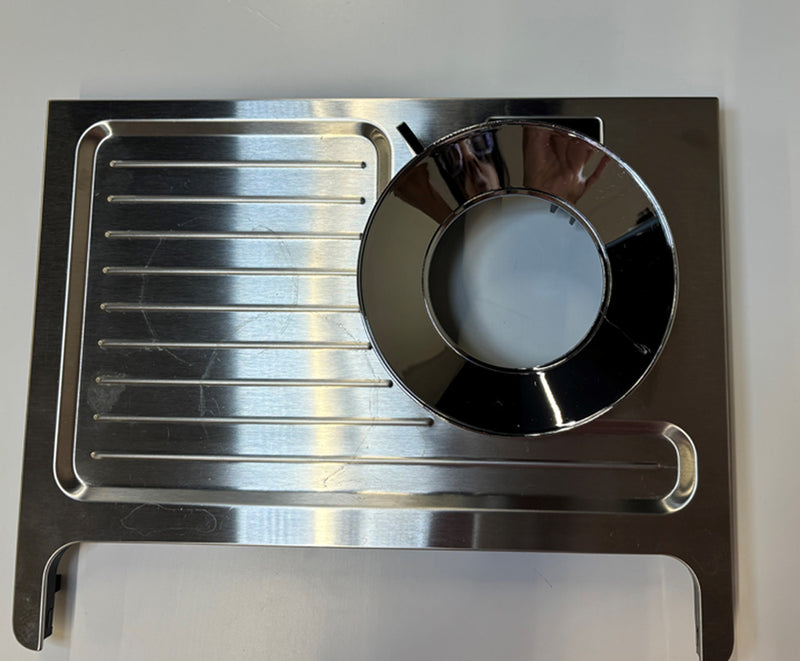 The DeLonghi Parts: Cover Assembly AS00002423, designed for the La Specialista Prestigio coffee machine, features a circular opening on the right for a cup holder and grooves on the left for collecting drips. This cover assembly has a reflective stainless steel surface and is presented against a white background.