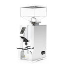 Image of a polished chrome Eureka Oro Mignon Dolce Vita coffee grinder by Eureka with a clear, rectangular bean hopper on top. The front features a digital display and control buttons, positioned above the coffee grounds dispenser. The grinder, equipped with Pure Diamond Burrs and Silent Technology, has a sleek, modern design.