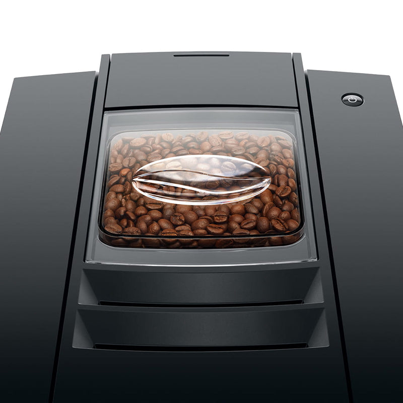 A close-up view of the Jura E8 Piano Black Automatic Coffee Machine 15648 (Latest Version)'s bean hopper filled with coffee beans. The beans are visible through a transparent lid on the top of the machine. The dark, sleek exterior of the Jura E8 is partially visible around the hopper, promising barista-quality coffee with every brew.