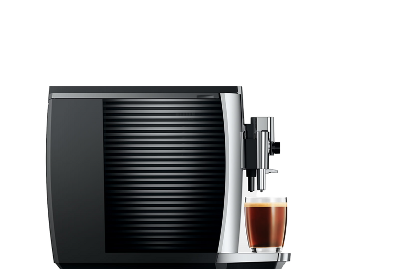 A sleek, chrome Jura E8 Chrome Automatic Coffee Machine 15646 (Latest Version) with ribbed side panels is dispensing a freshly brewed espresso into a glass mug. The machine is photographed against a plain, dark background, highlighting its modern design and barista-quality coffee experience from Jura.