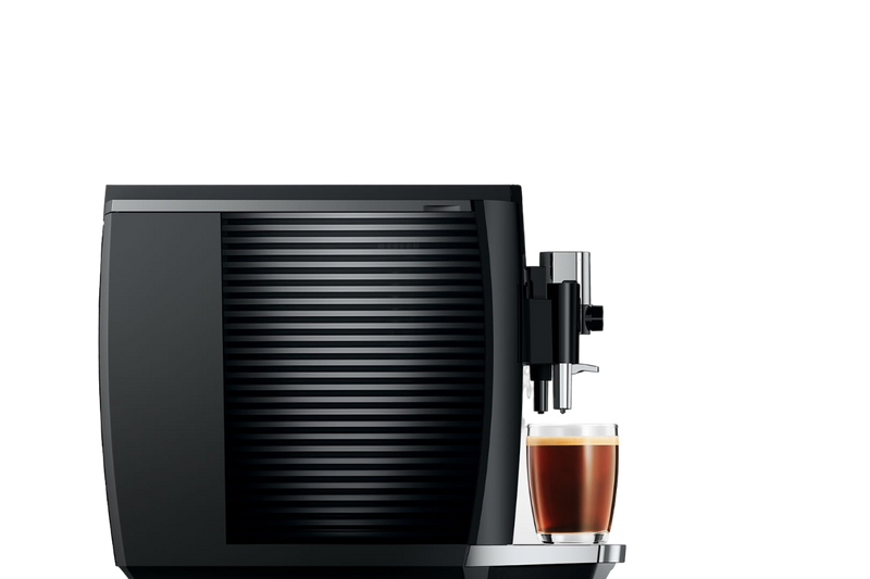 Side view of a sleek JURA E8 Piano Black Automatic Coffee Machine 15648 (Latest Version) with a ribbed design, dispensing a fresh cup of barista-quality coffee into a clear glass. The machine boasts minimalist aesthetics, and the glass showcases the distinct layers of coffee and crema.